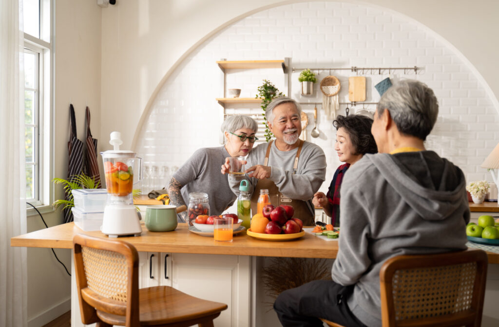A group of older adults standing around a kitchen island that's filled with fruits, vegetables, and a blender. One woman is smelling fruit juice as a man holds the glass.