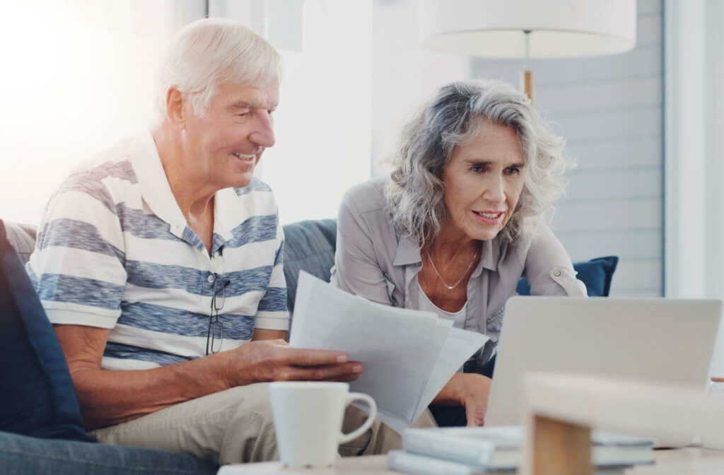 An older couple smiling while sorting through paperwork and researching potential senior living communities.