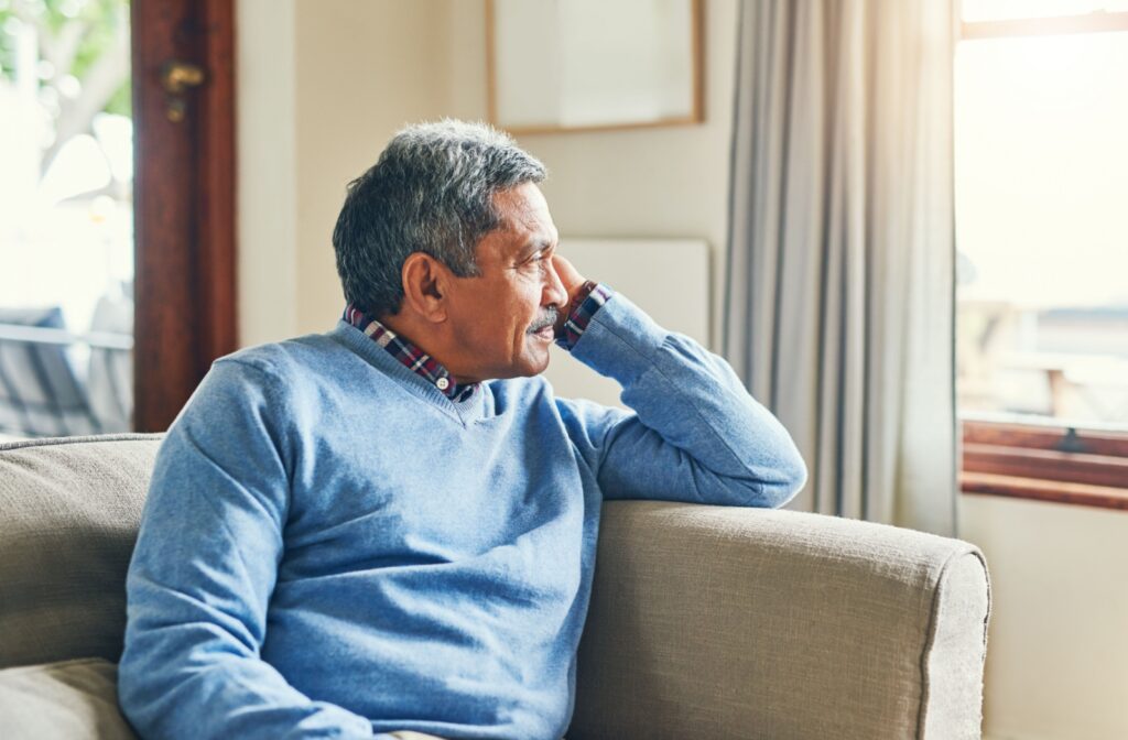 An elderly man sitting on the couch and looking out the window.